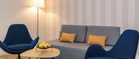 A modern living room with a grey sofa, two blue armchairs, a small wooden coffee table with fruit, and a floor lamp.
