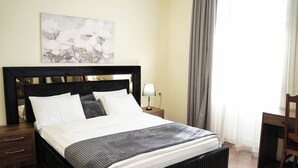 Una cama bien tendida con una colcha a rayas, una mesita de noche con una lámpara y un cuadro en la pared.