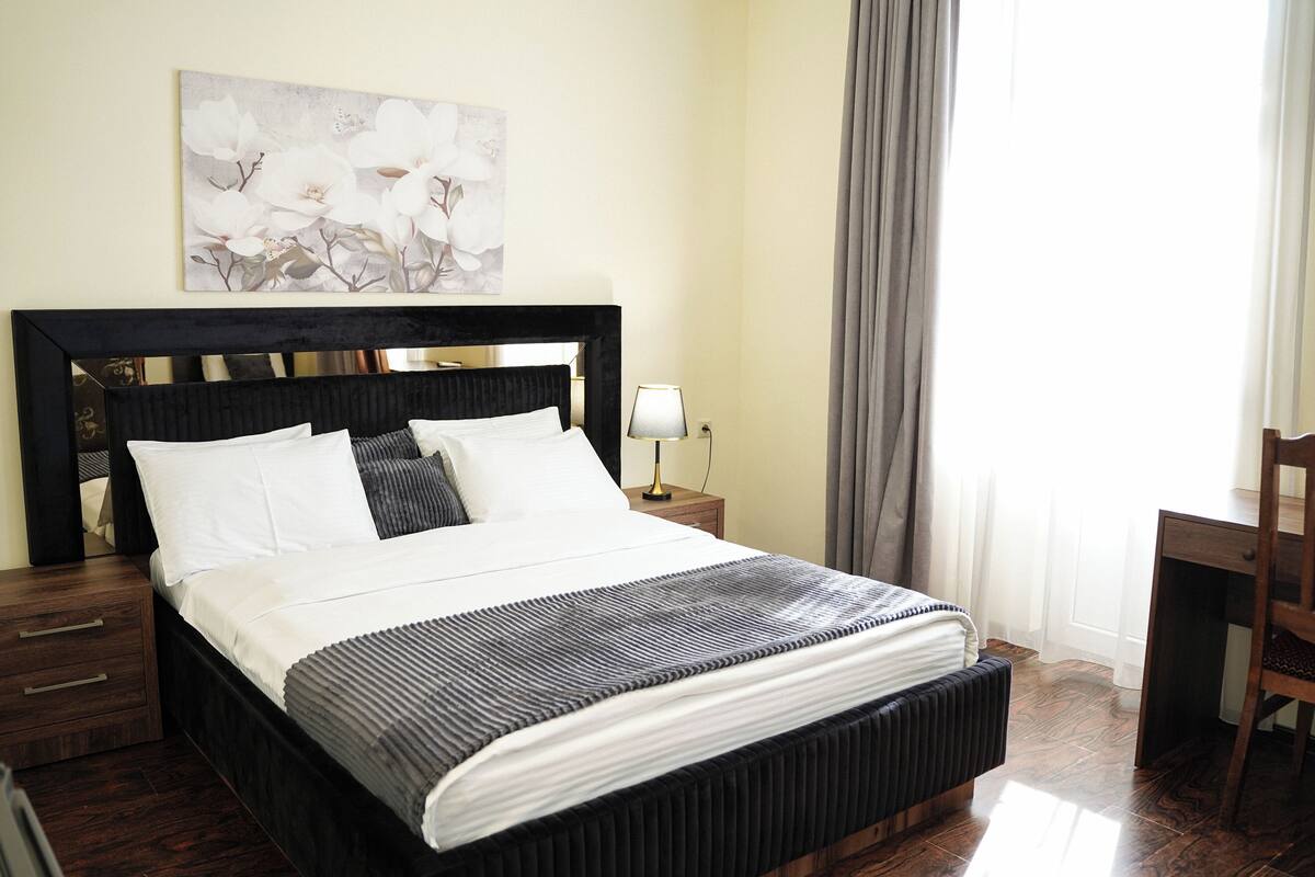 A neatly made bed with a striped bedspread, a bedside table with a lamp, and a painting on the wall.