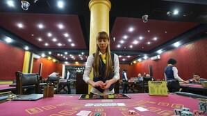 Una mesa de casino con un crupier, un juego de blackjack en curso y un cartel de Crystalbet.
