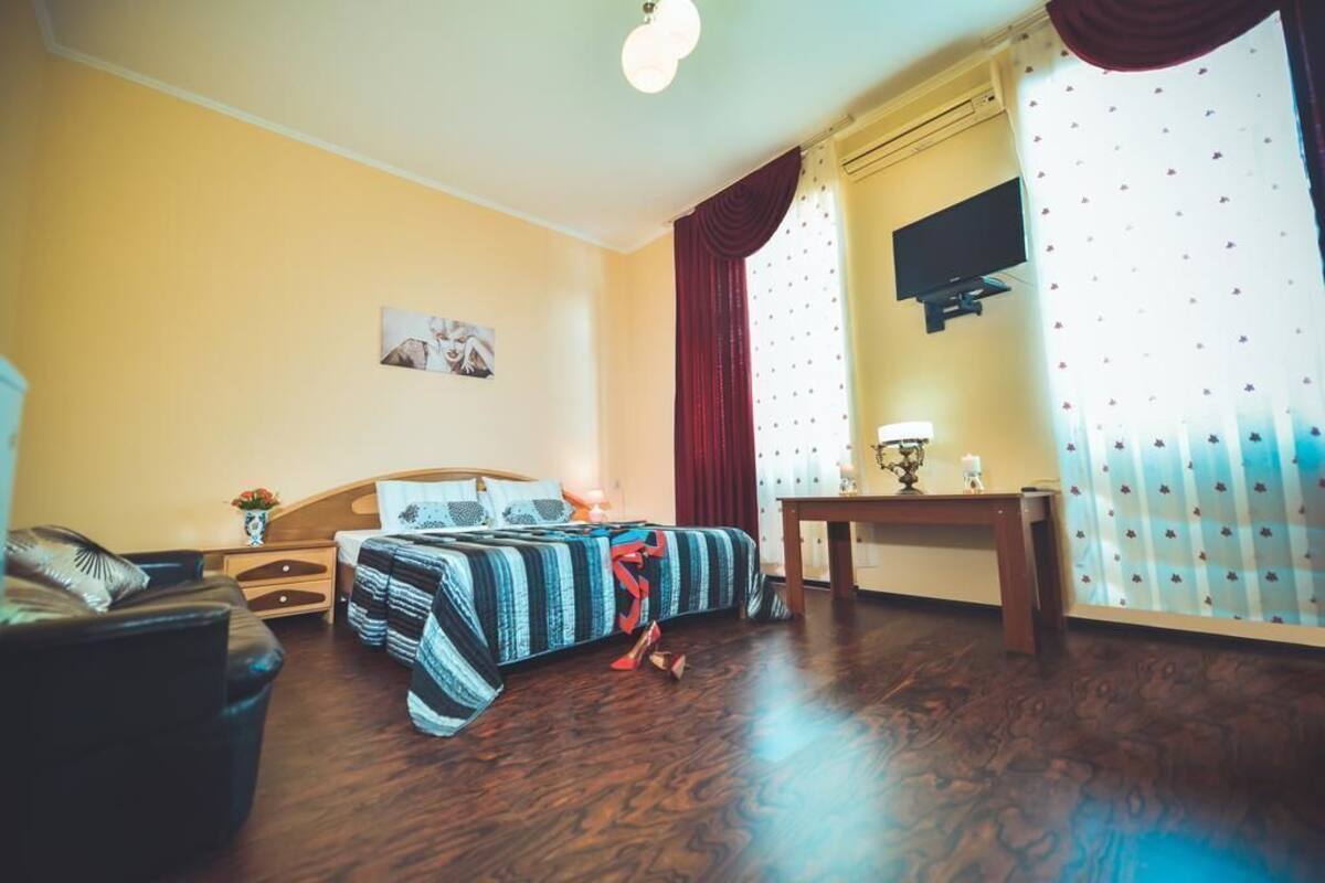 A hotel room with a bed, a nightstand, a table, a TV, and curtains.