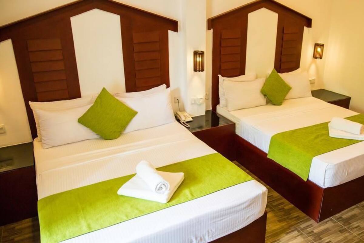 Two twin beds with wooden headboards, green bedspreads, and white bedding. Each bed has a bedside table with a lamp and a telephone.