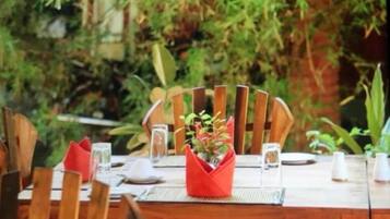 A wooden dining table set outdoors with chairs, a red centerpiece, and a natural backdrop.