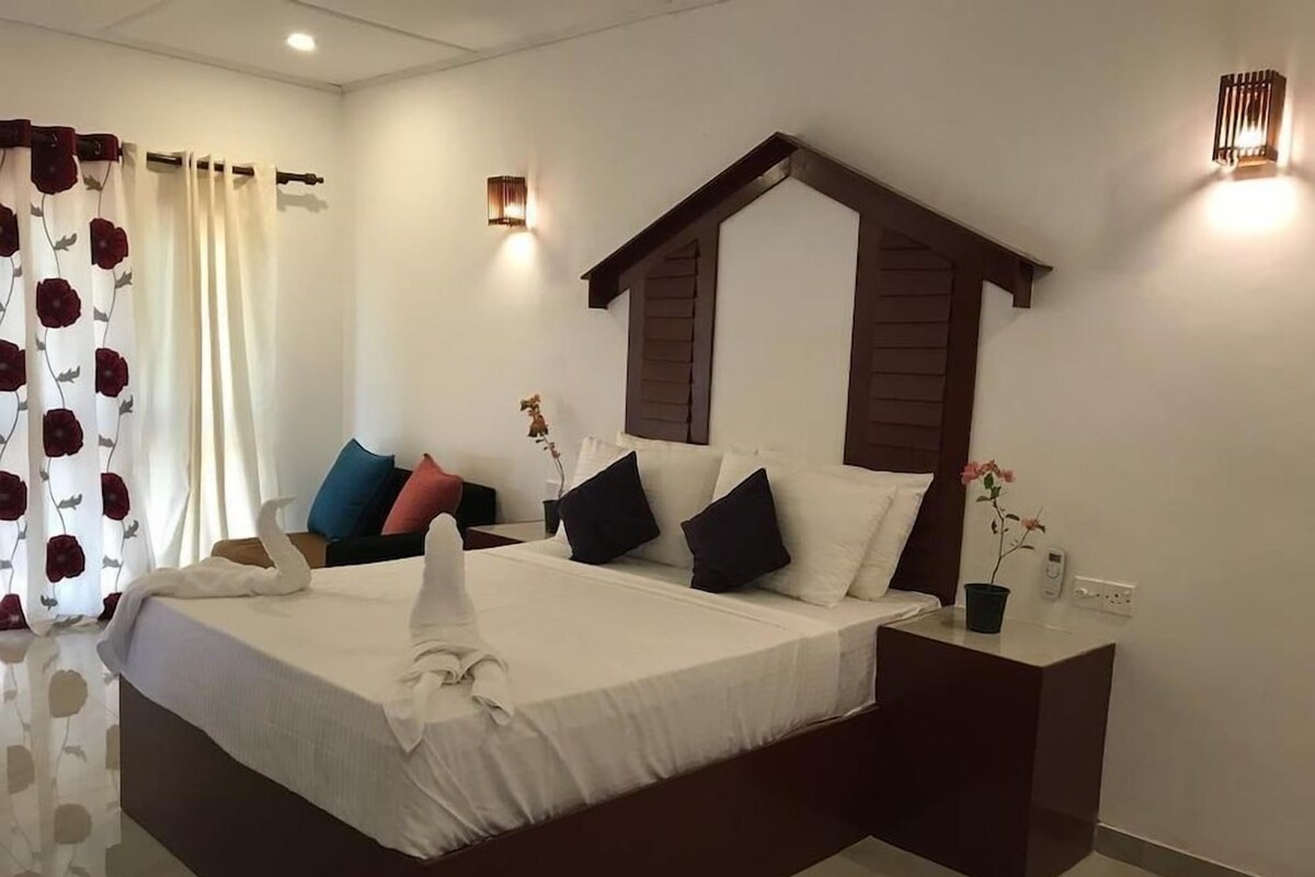 A hotel room with a large bed, a nightstand, a wall-mounted lamp, and a window with curtains.