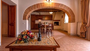 A dining area with a table set for two, a floral centerpiece, and a brick archway leading to a kitchen. - Agriturismo Concadoro (Castellina in Chianti)
