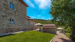 A stone building with a tiled roof, a well-maintained lawn, and a small patio area with outdoor furniture. - Agriturismo Concadoro (Castellina in Chianti)