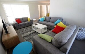 Relax in this stylish living room with a sofa, coffee table, and TV, surrounded by a large window and a colorful rug.