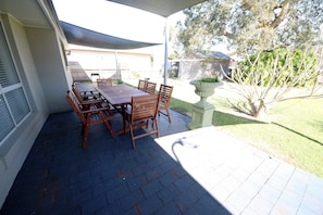 Enjoy dining or socializing in this serene outdoor space with a shaded patio, lawn, and tree.