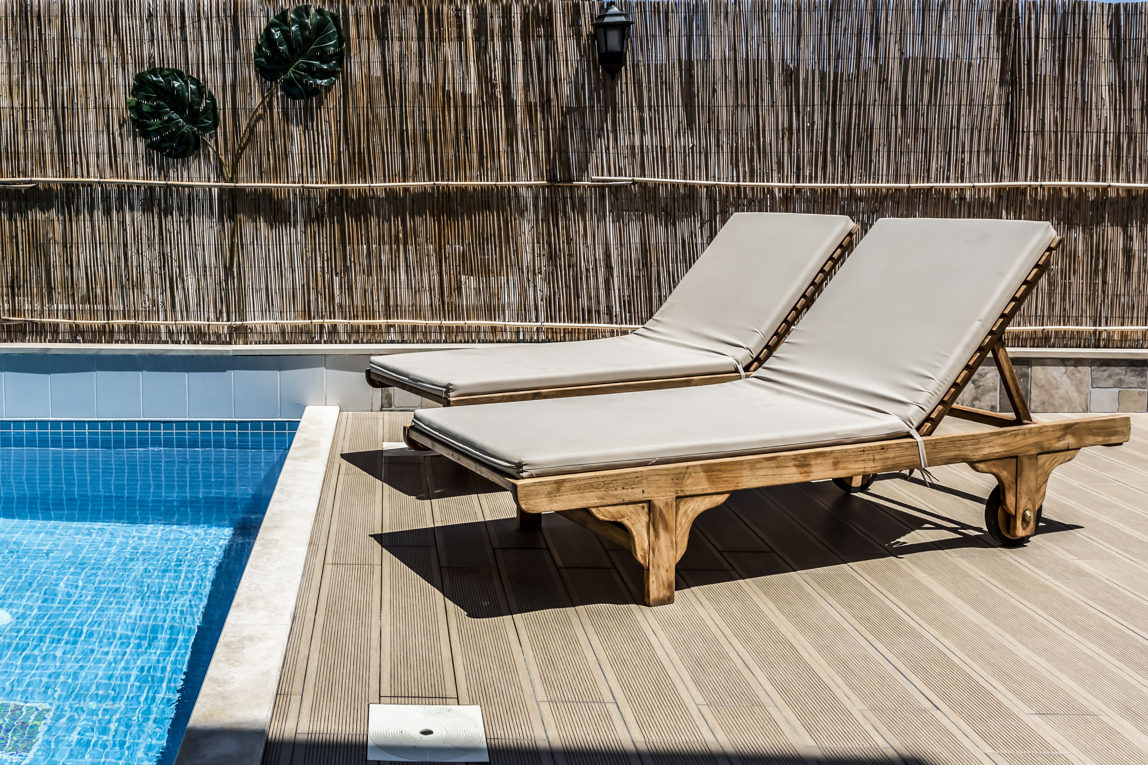 A poolside area with two wooden lounge chairs and a bamboo wall.