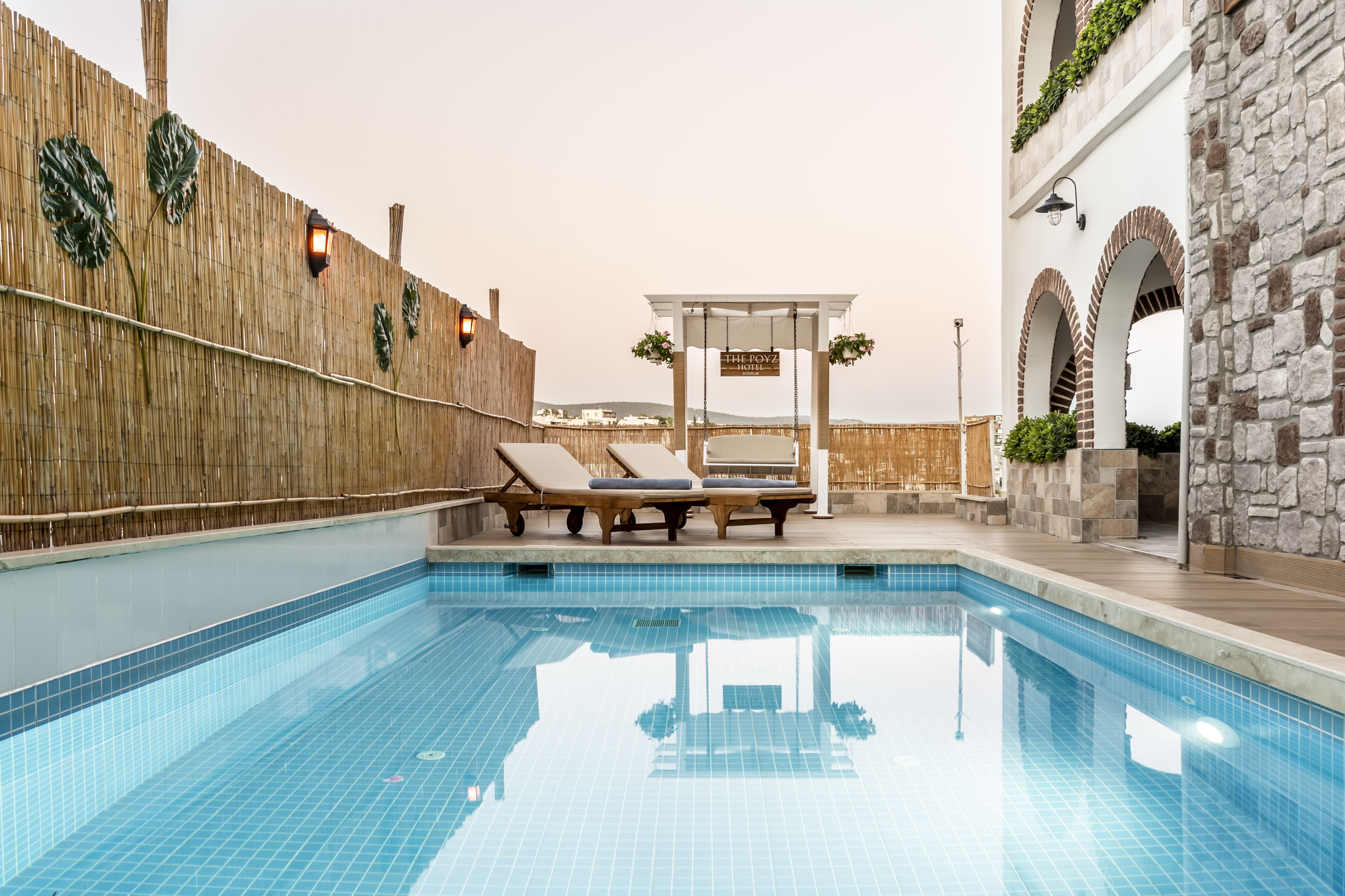 A pool area with lounge chairs, a wooden fence, and a stone wall.