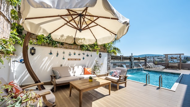 A sunlit outdoor seating area with a pool, wooden furniture, and a large umbrella. - The Poyz Hotel Bodrum (Bodrum)