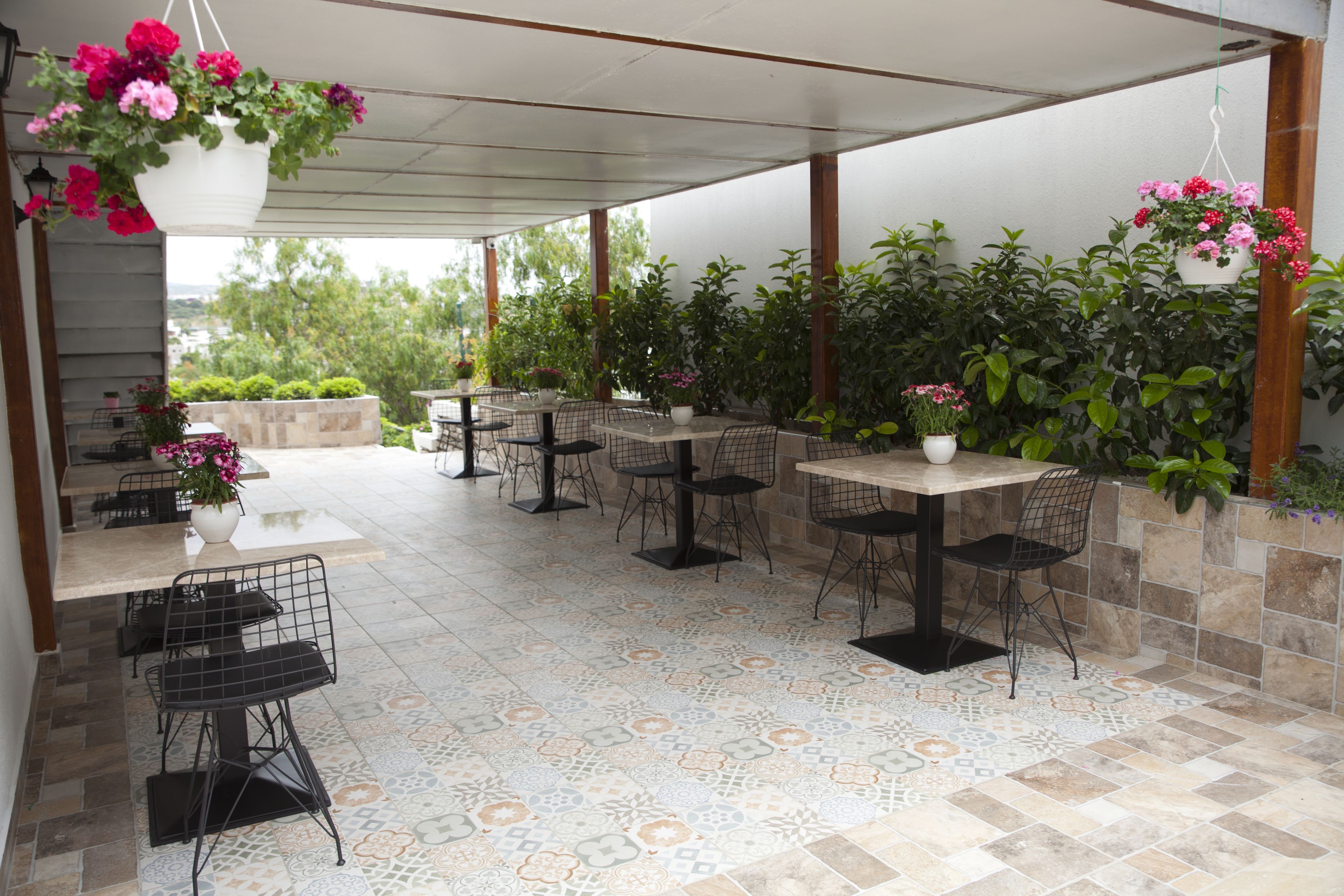 An outdoor patio area with tiled flooring, multiple tables and chairs, and hanging flower baskets.