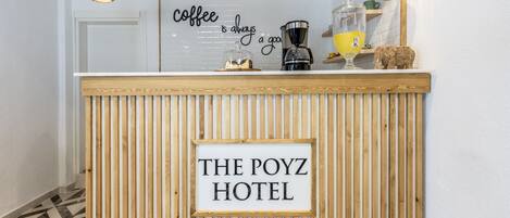 Una reception dell'hotel The Poyz con un cartello che recita "il caffè è sempre una buona idea" e una macchina da caffè.