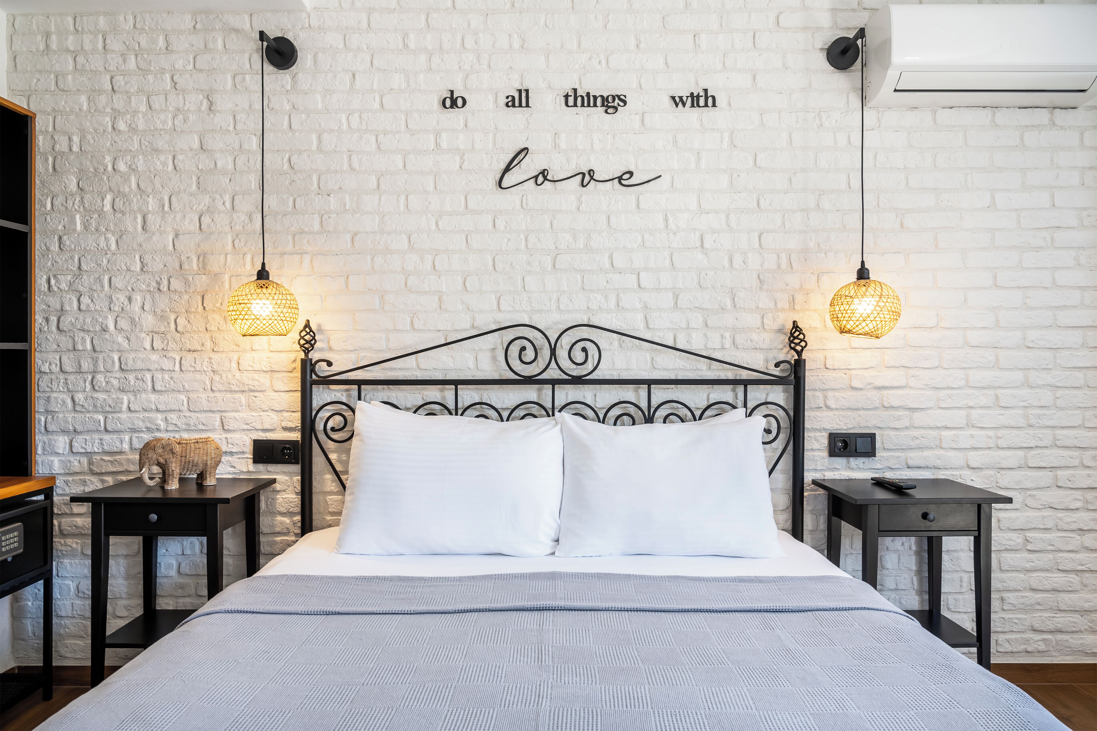 A neatly made bed with white linens, two bedside tables with lamps, a decorative elephant figurine, and a wall with a motivational quote.