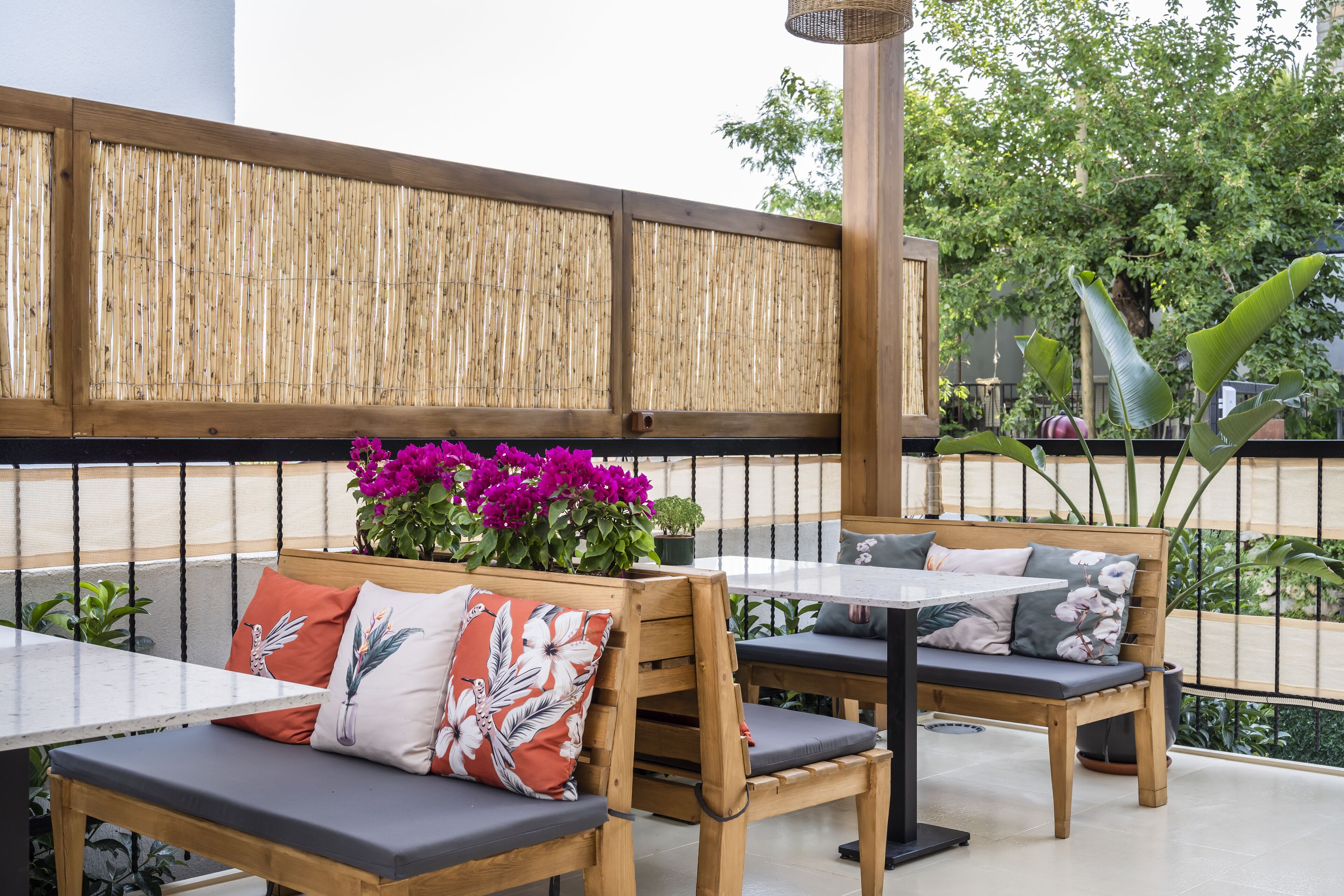 A wooden bench with cushions, a table, and a bamboo fence in a patio area.