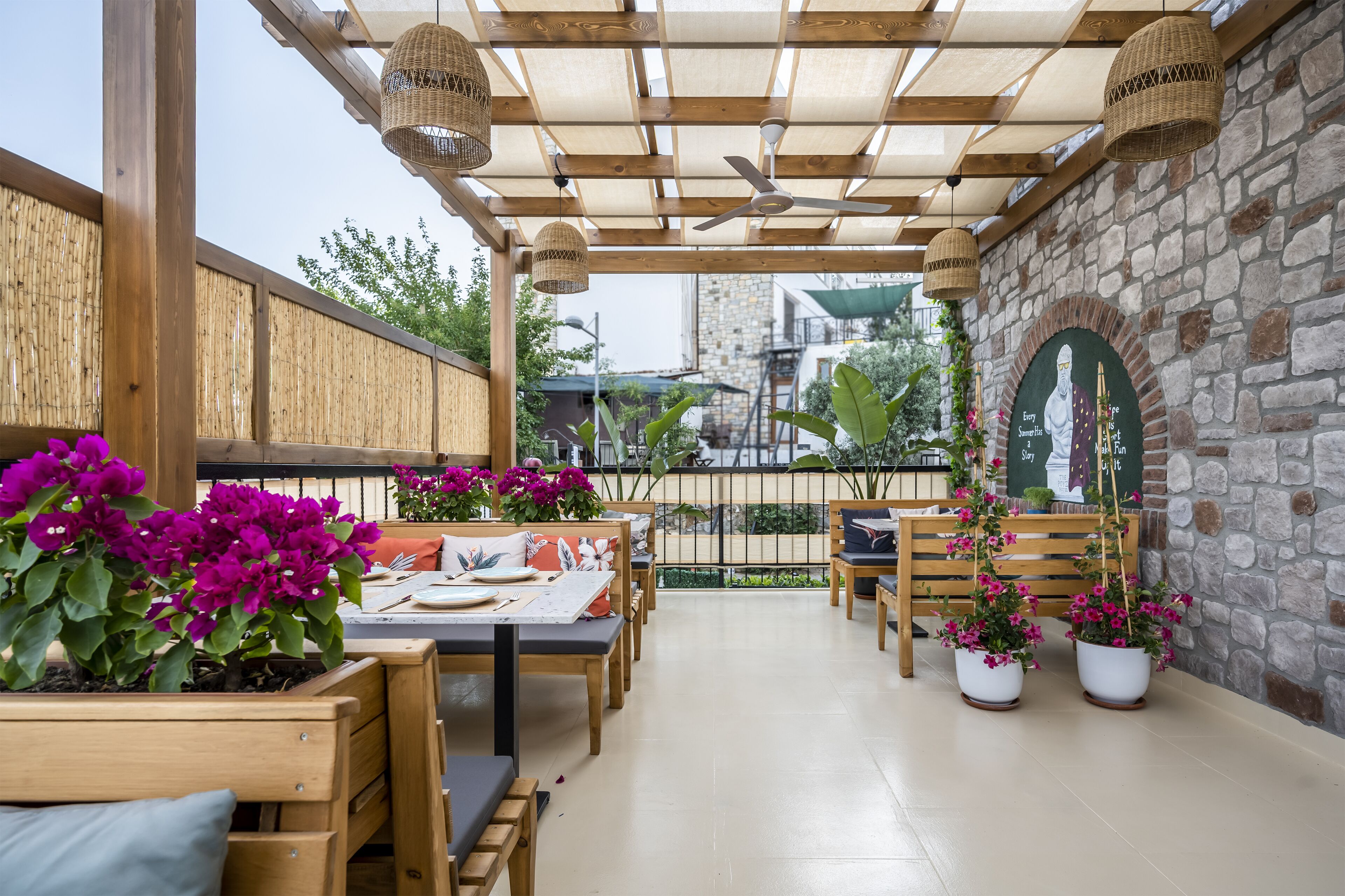 An outdoor patio with wooden tables and chairs, potted plants, and a stone wall.