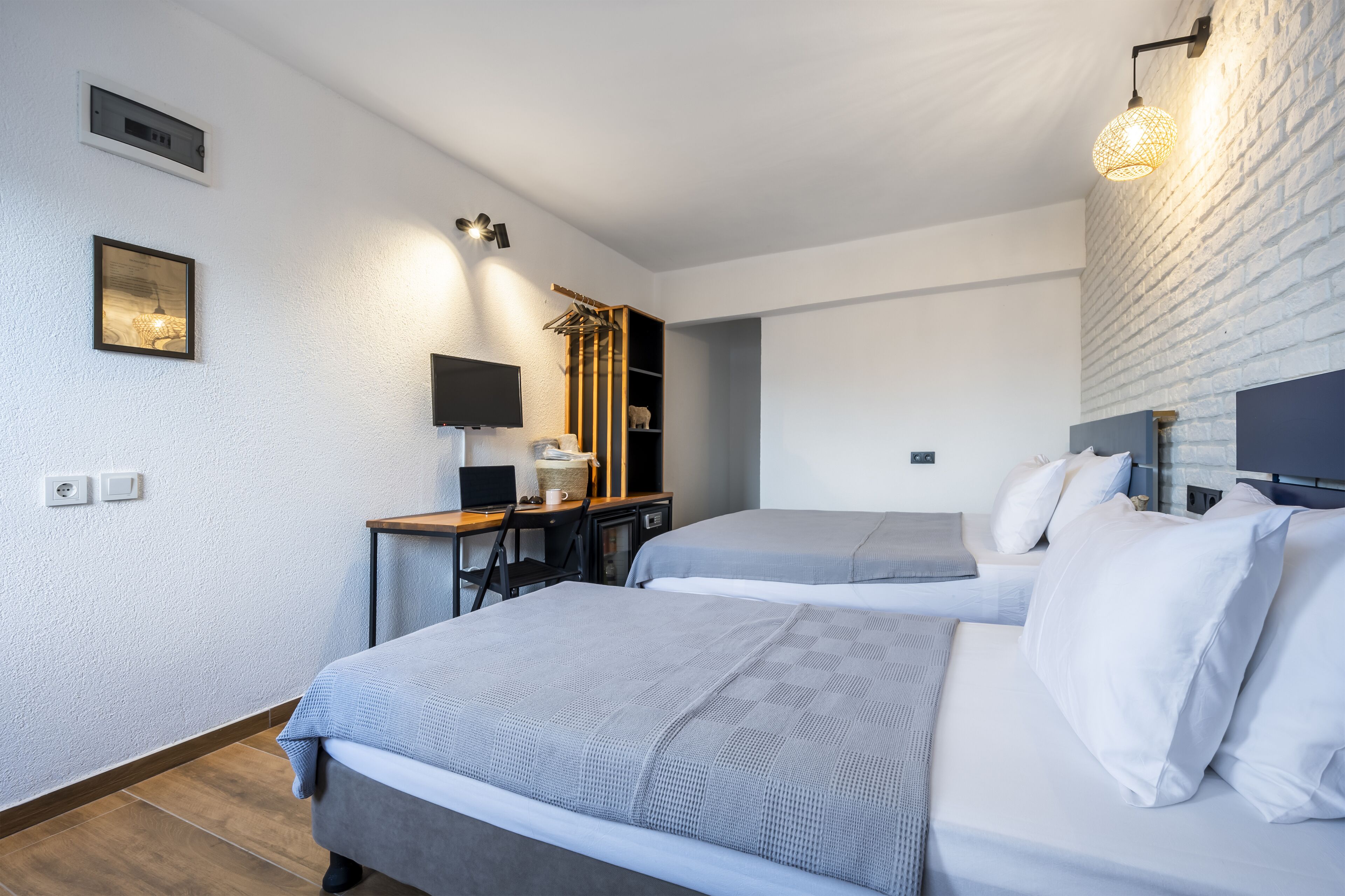 A modern hotel room with two beds, a desk, a chair, a TV, and a wardrobe.