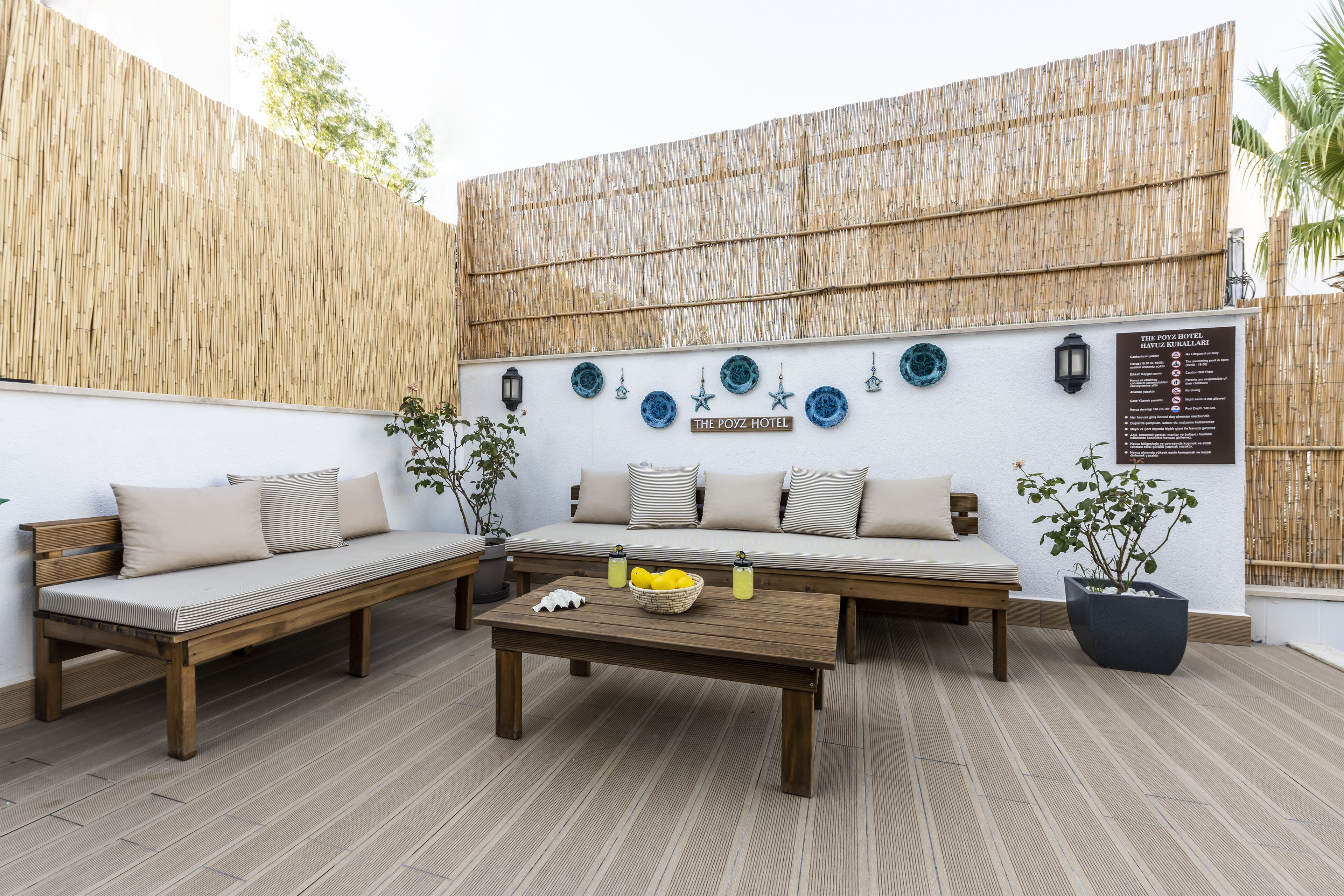 A patio area with a wooden bench, a sofa, and a coffee table. There are decorative plates on the wall and a sign for The Poyz Hotel.