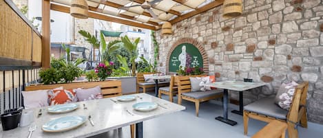 Un café al aire libre con paredes de piedra, muebles de madera y luces colgantes.