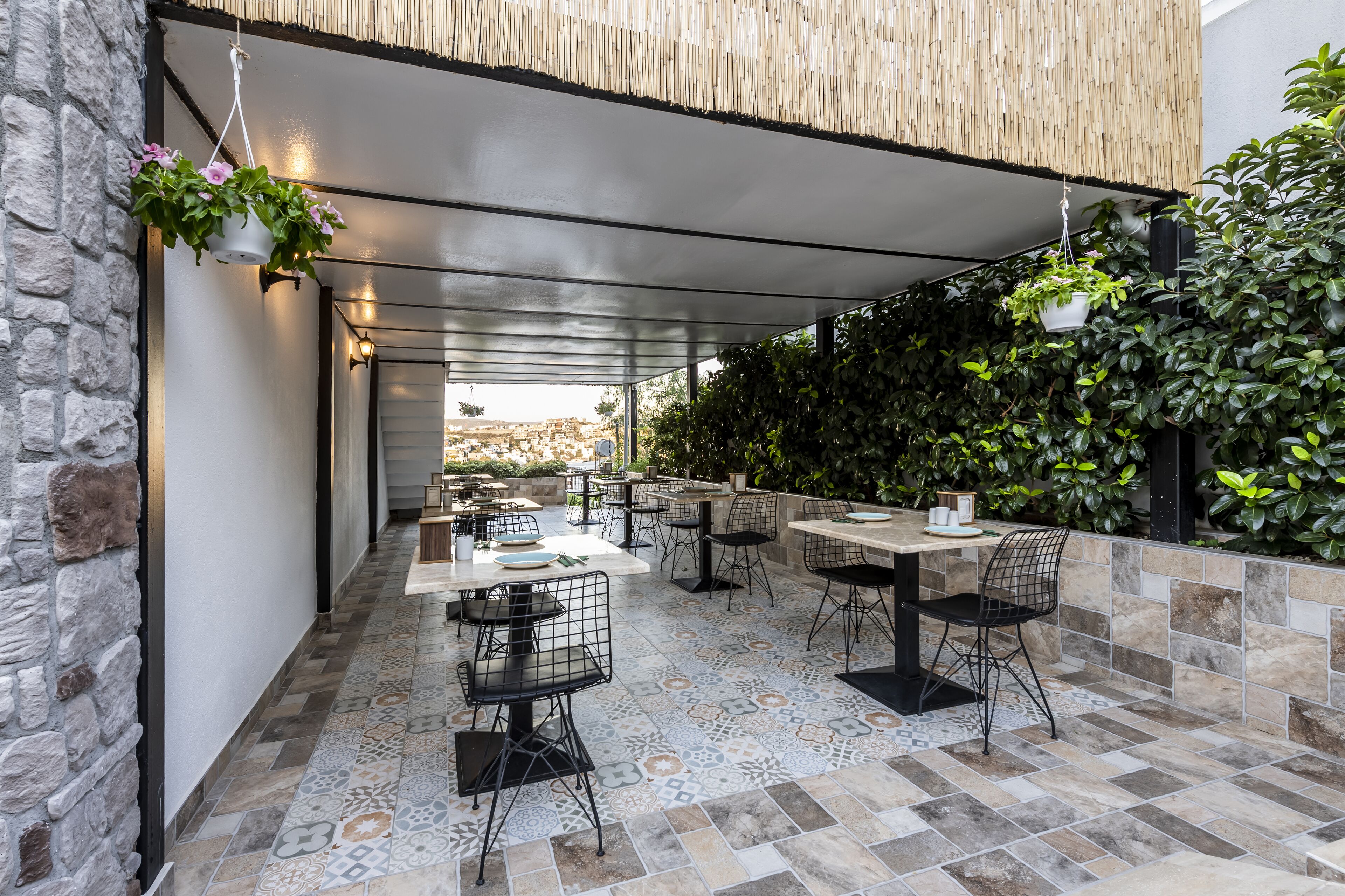 Un espacio al aire libre con mesas y sillas, un muro de piedra y plantas colgantes.