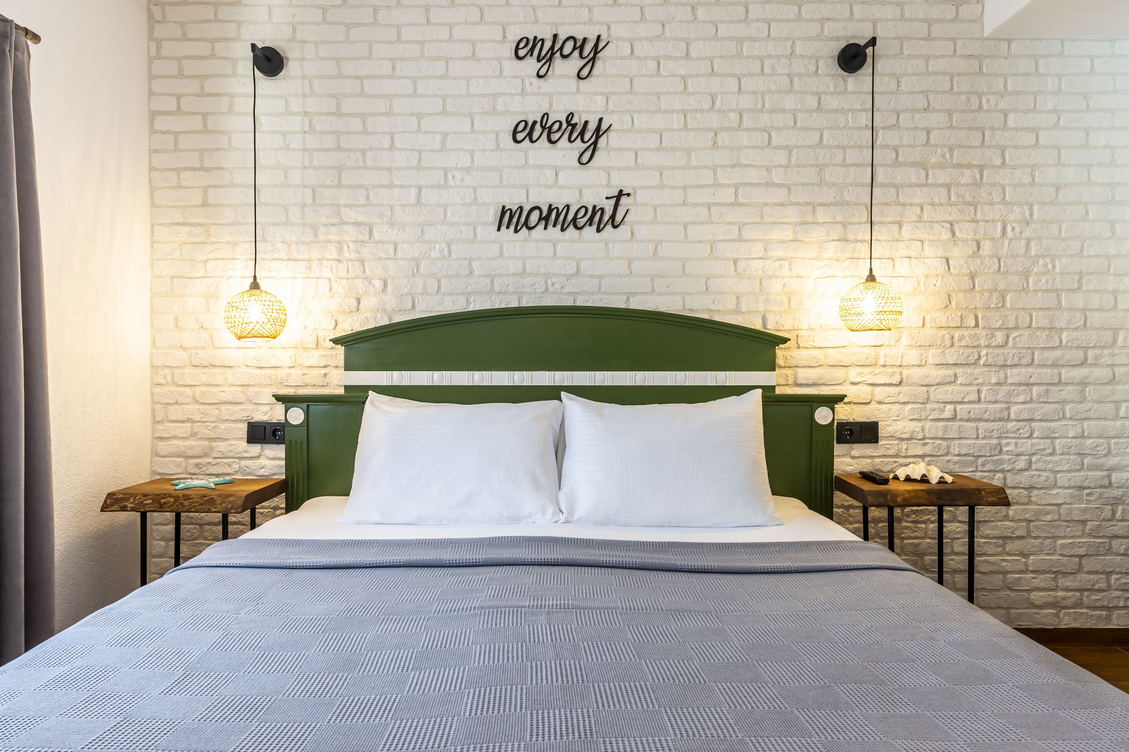 Una cama bien hecha con un cabecero verde, dos mesitas de noche con lámparas, y una pared con una cita motivacional.