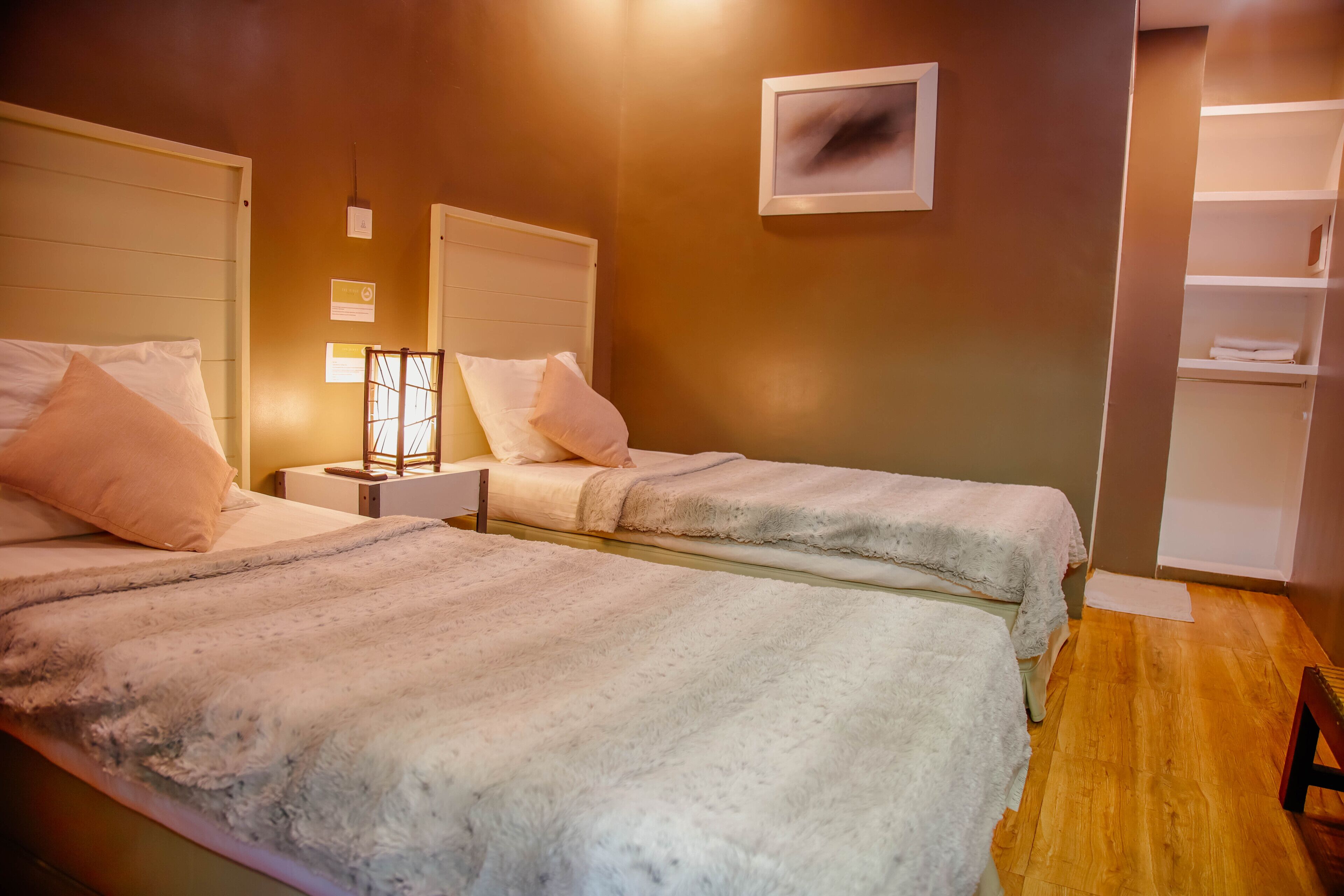 A room with two beds, a nightstand, a wall-mounted shelf, and a wooden floor.
