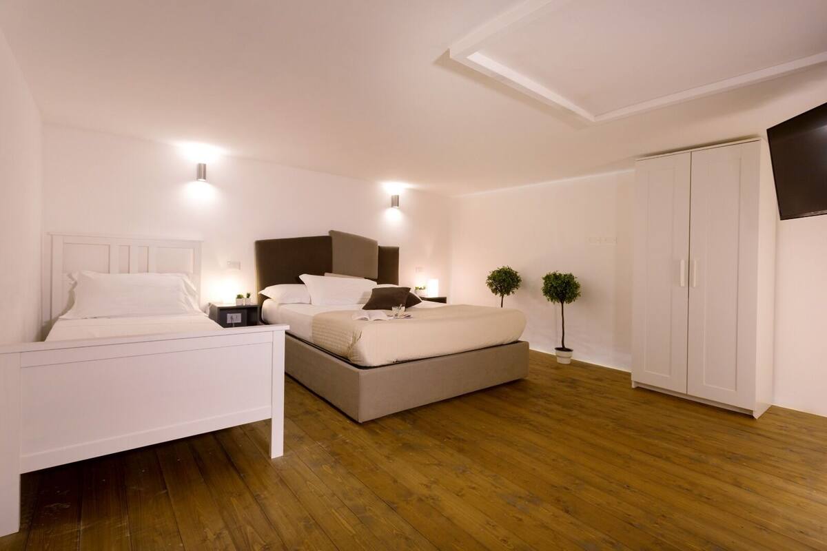 Un dormitori amb un llit, taules de nit, un armari i dues plantes en testos.