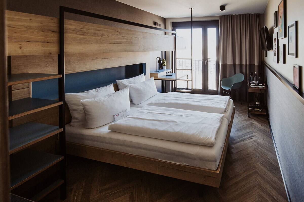 A modern hotel room with a large bed, built-in shelving, a desk, and a balcony with a view.