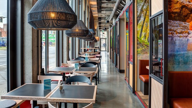 Un restaurante con mesas y sillas dispuestas a lo largo de un pasillo con amplios ventanales.
