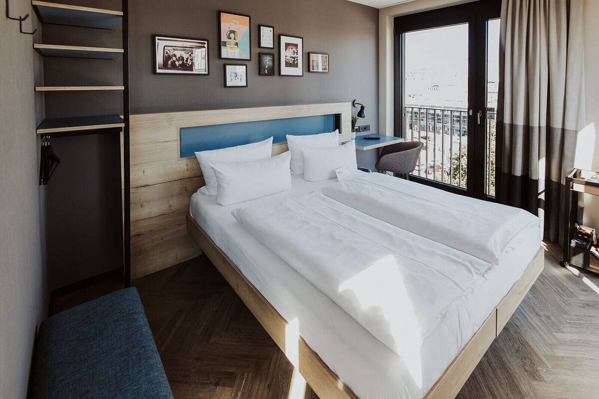 A hotel room with a large bed, a desk, a chair, and a balcony with a view.
