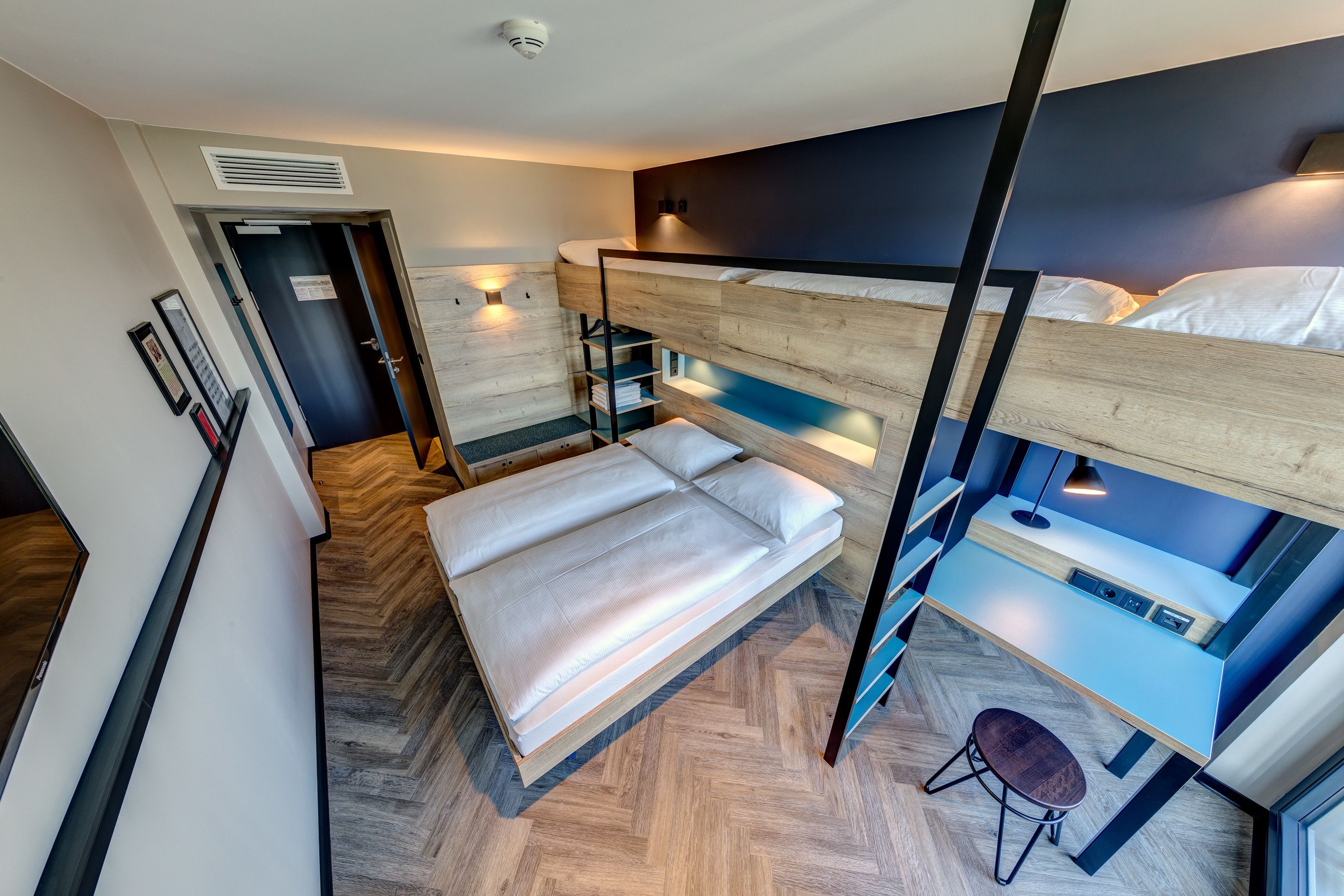 A bunk bed room with a desk and chair, a heater, and a wall-mounted shelf.