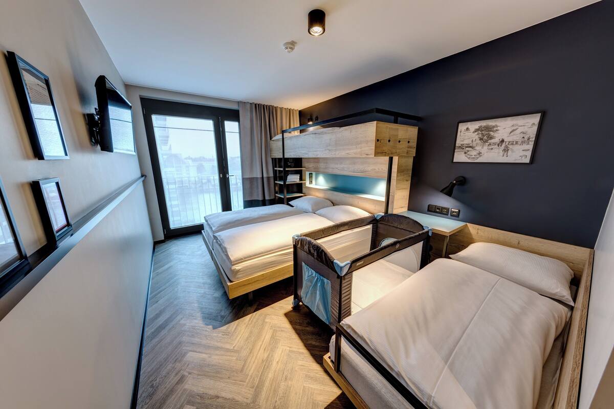 A modern hotel room with bunk beds, a desk, and a large window offering a city view.