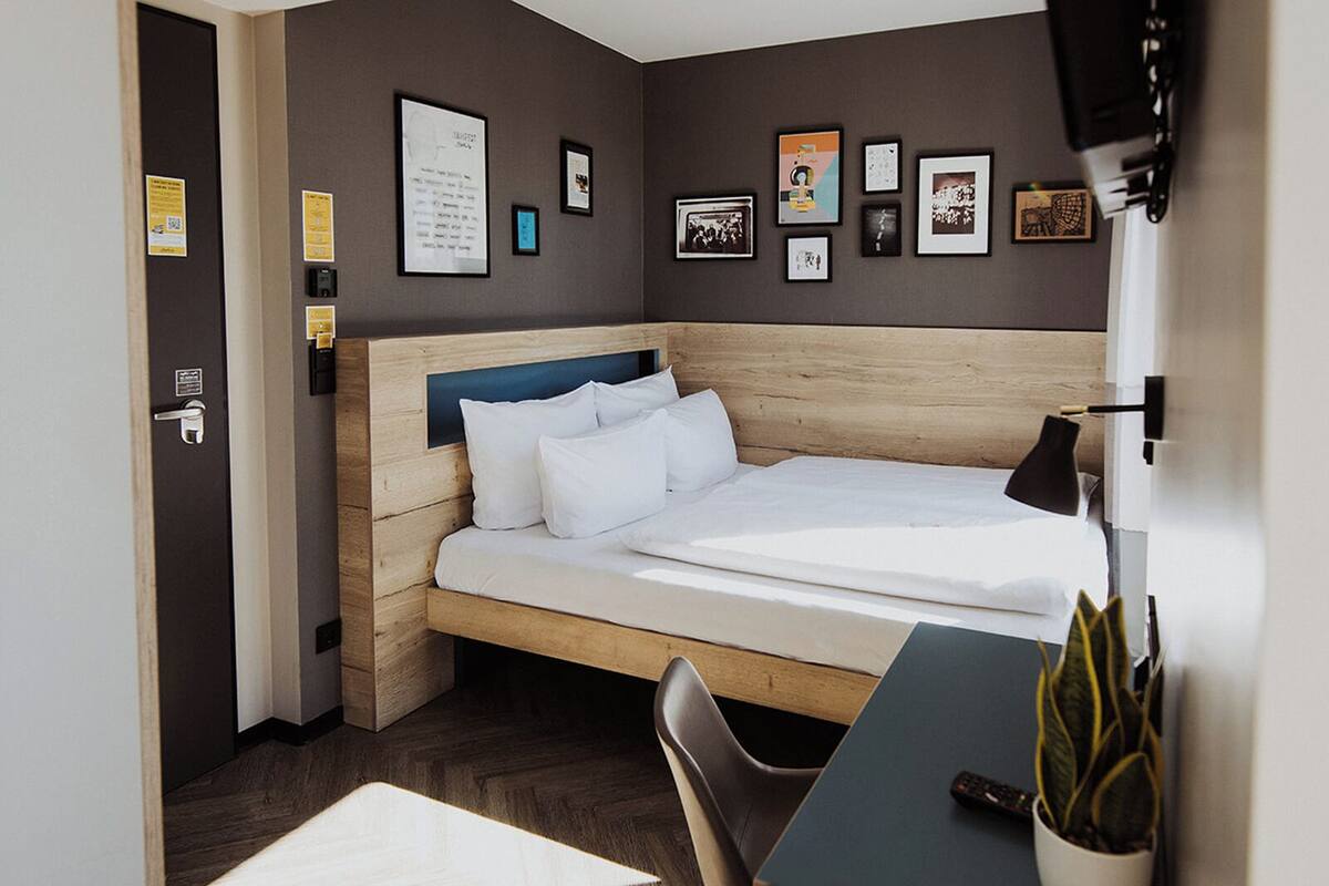 A single bed with a wooden headboard, a desk with a chair, and a potted plant.