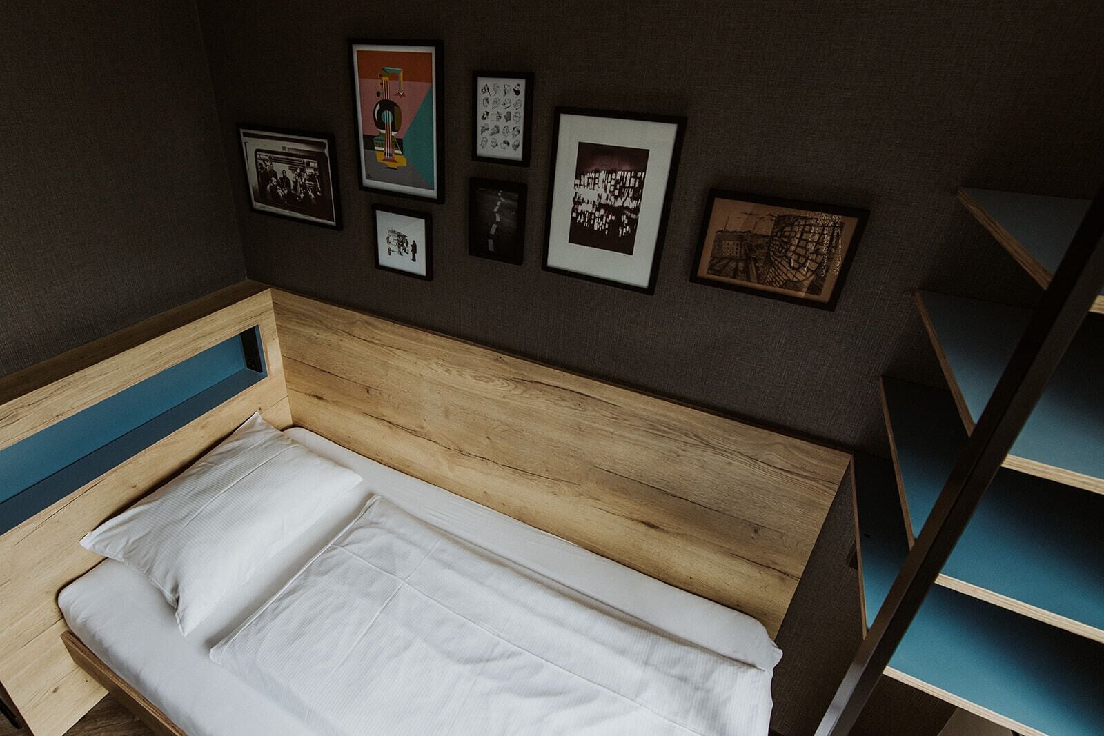 A small, single-bed room with a wooden headboard and a blue shelf unit.