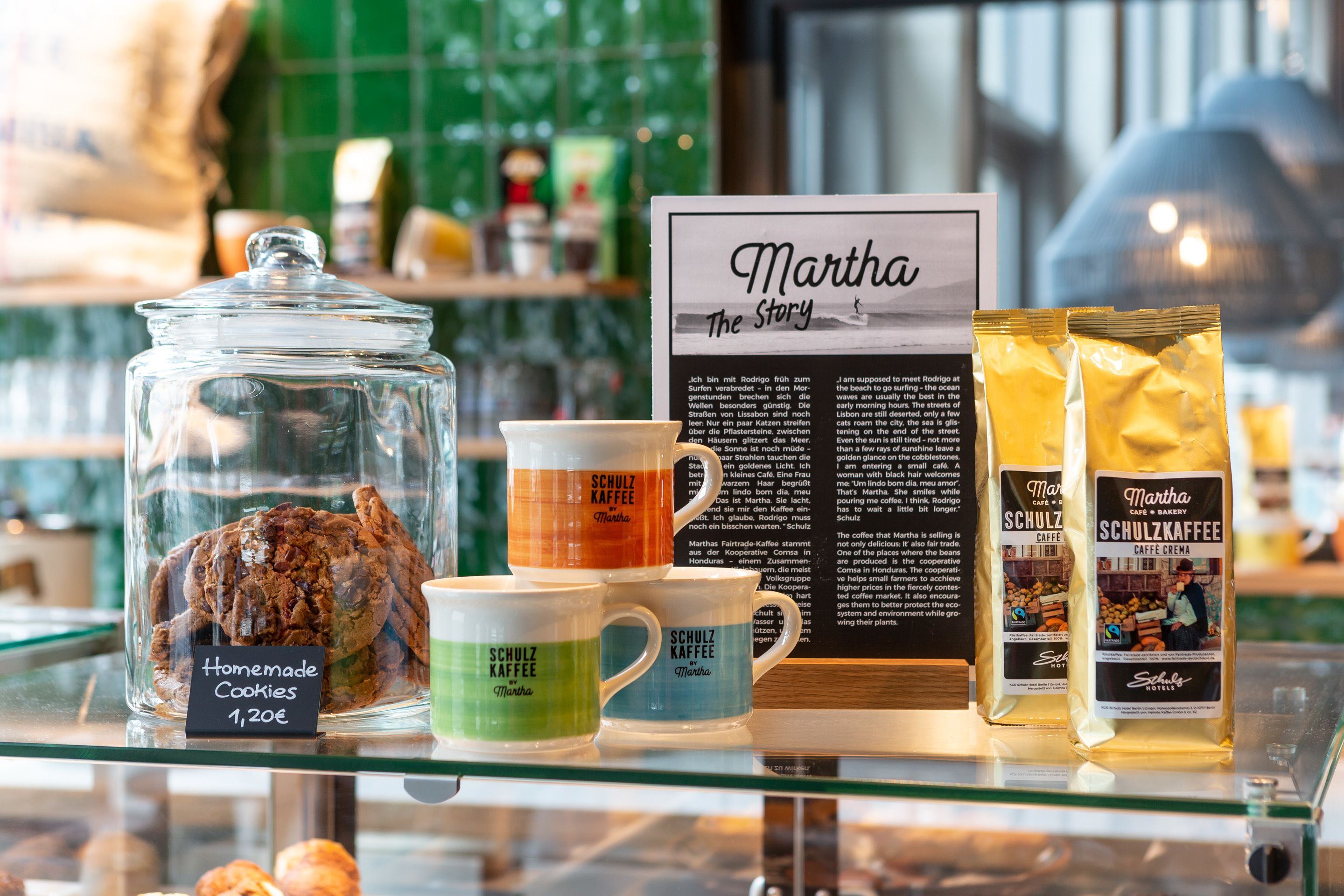 Eine Präsentation von Martha Kaffee-Produkten, darunter Tassen und Kaffeebeutel, zusammen mit einem Glas selbstgemachter Kekse.