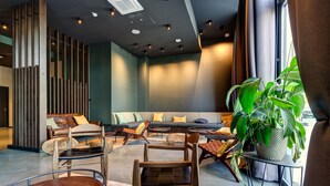 Un espacio lounge moderno con arreglos de asientos, una planta grande en maceta e iluminación empotrada en el techo.