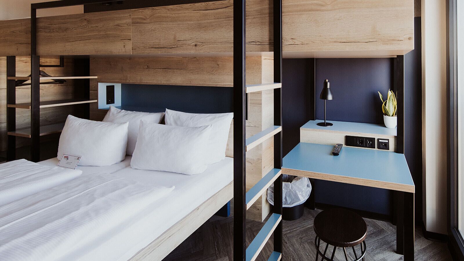 A bunk bed with a desk and chair, a small trash bin, and a potted plant.