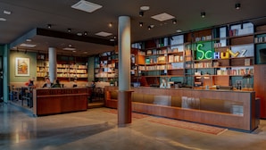 Un área de auto-check-in con un mostrador de recepción de madera, una amplia estantería llena de libros y un letrero de neón que dice