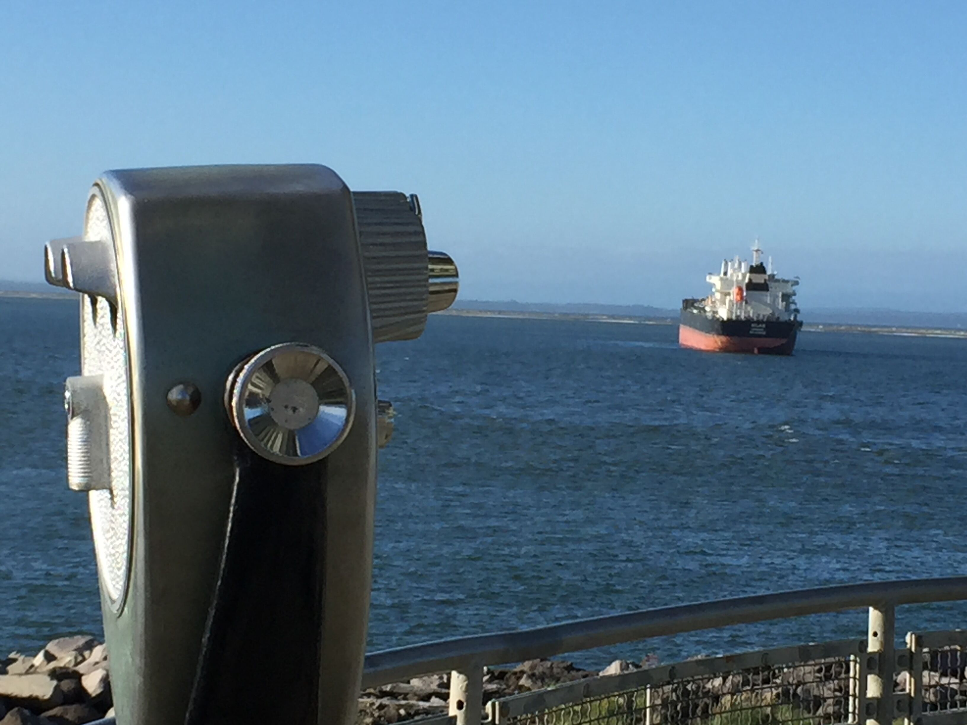 A large ship on the water, viewed from a metal structure with a railing in the foreground.