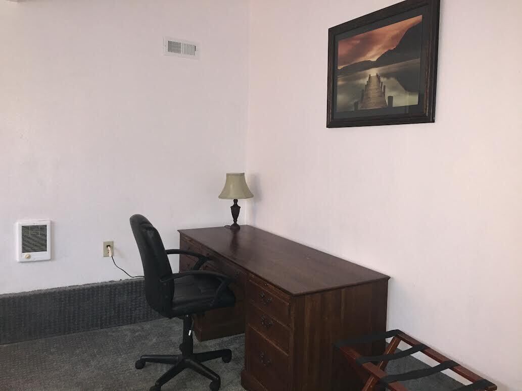 Une pièce avec un bureau en bois, un fauteuil de bureau noir, une lampe et un tableau encadré accroché au mur.