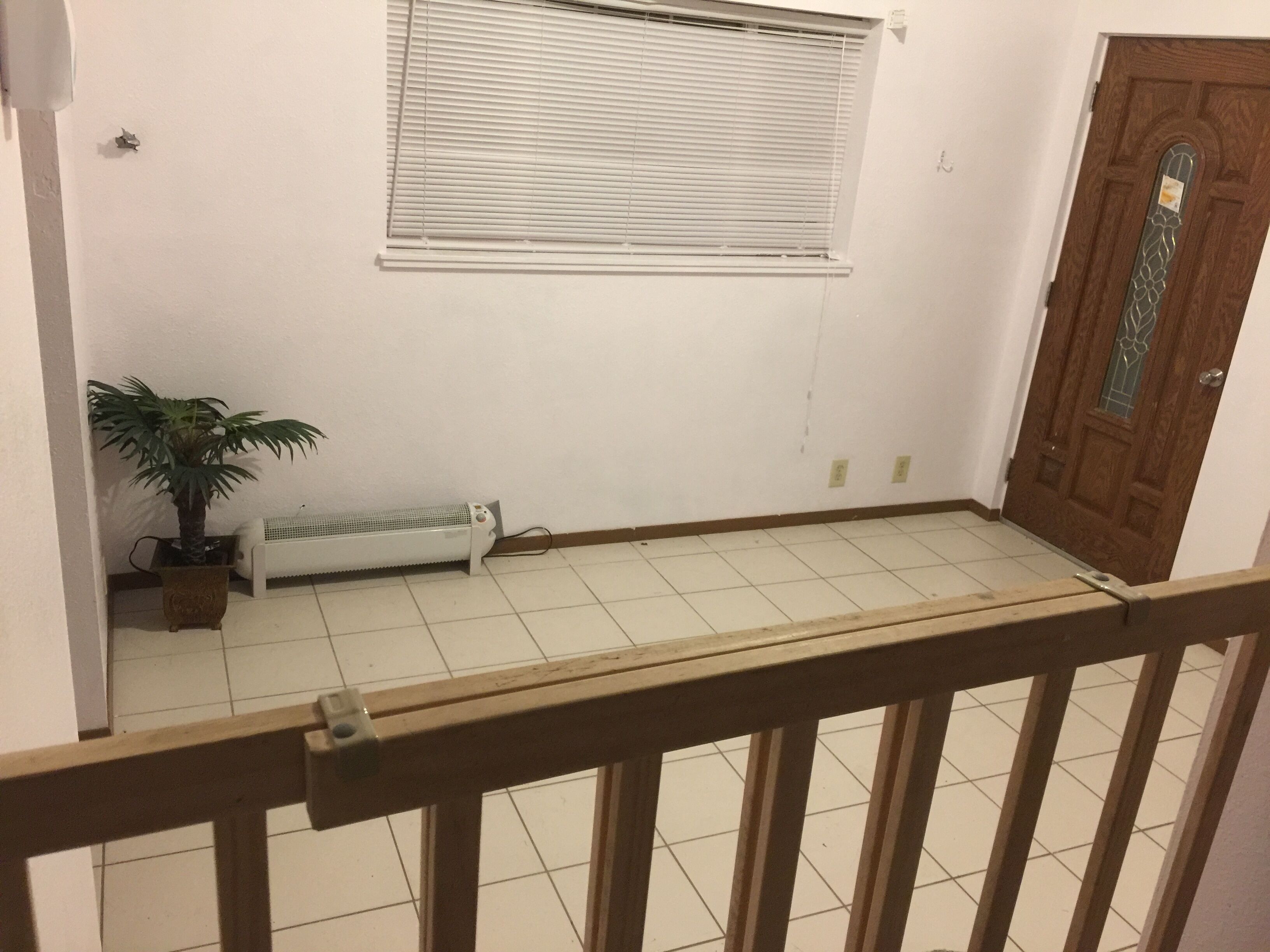 Une pièce avec un radiateur, une plante en pot, une fenêtre avec des stores et une porte en bois.