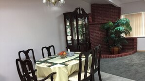 A dining area with a round table covered by a tablecloth, surrounded by wooden chairs. A glass bowl with fruits is on the table, and a mirror hangs on the wall. - Large Vacation Home (1878sf) near Beach, WiFi, SmartTV, Bikes, fishing gears (Westport)