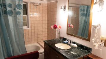 A bathroom with a white bathtub, a sink with a black countertop, and a mirror above the sink.