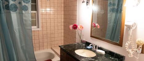A bathroom with a white bathtub, a sink with a black countertop, and a mirror above the sink.