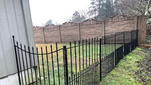 A black metal fence with a decorative top rail, a stone wall with carved figures, and a grassy area with fallen leaves. - Large Vacation Home (1878sf) near Beach, WiFi, SmartTV, Bikes, fishing gears (Westport)