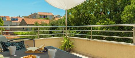 A balcony with a table, chairs, a potted plant, and a white umbrella.