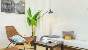 Een woonkamer met een bank, een fauteuil, een tafel, een vloerlamp, een kamerplant en een ingelijst schilderij aan de muur.
