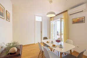 Un coin repas avec une table blanche, des chaises, un saladier de fruits et une tasse à café.