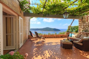 A sunlit patio with a view of the sea, wicker furniture, and a stone wall. - Hedera Estate, Hedera A13 (Dubrovnik)