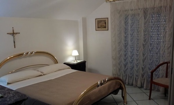 A bedroom with a bed, bedside table, lamp, chair, and a cross on the wall. - B&B Veronica (Baronissi)